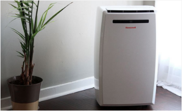A picture of a small portable Honeywell air conditioner sitting on the floor in the corner of the room.