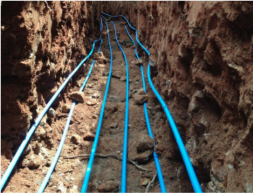 Several geothermal hydronic tubes are places in a deep trench and ready to be buried for a home installment.