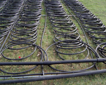 An image of many lines of geothermal laid out on the ground in slinky form, getting ready to be placed in a dug trench.